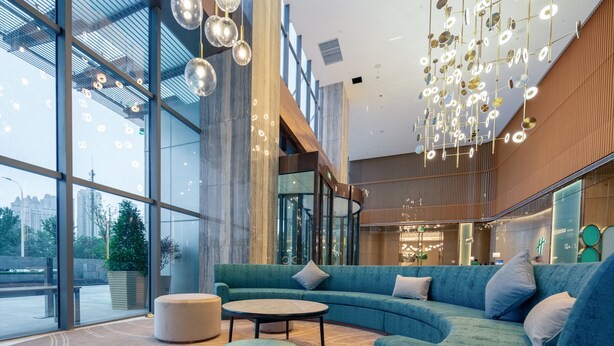 A modern lobby with a curved blue sofa, a round table, and hanging spherical lights.
