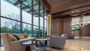 A modern lobby with large windows, a seating area with sofas and tables, and a view of the city skyline.
