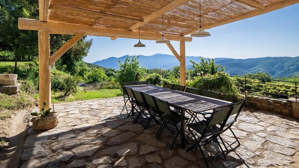 En udendørs terrasse med et træpergola, stengulv og et bord med stole.