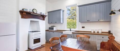 Una cocina con armarios blancos, estufa, microondas y una mesa de comedor con sillas.
