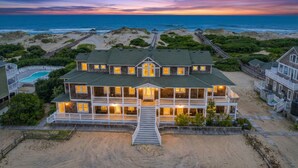 A large, multi-story beachfront property with a prominent central building, a swimming pool, and a boardwalk leading to the beach. - Oceanfront Estate | 14BR | Private Pool & Hot Tub | Sleeps 32 (Corolla)