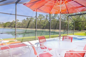 A covered outdoor area with a pool, lounge chairs, and a table. - Tropical Boho Lakefront Villa | Private Pool & Spa | Game Room | Near Disney (Kissimmee)