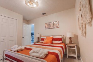 A neatly arranged bedroom with a bed, bedside tables, and a hanging macrame piece. - Tropical Boho Lakefront Villa | Private Pool & Spa | Game Room | Near Disney (Kissimmee)