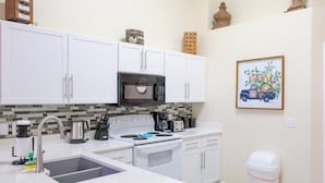 A modern kitchen with white cabinets, a stainless steel sink, a microwave, a stove, and a trash can.