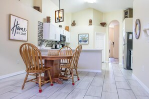 A dining area with a wooden table and chairs, a kitchen in the background, and a hallway leading to other rooms. - Fun Packed 5 Bedroom Villa with Private Pool/Spa, Games Room & Grill (Kissimmee)