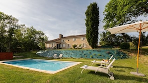 A pool with lounge chairs and a pergola in a backyard.