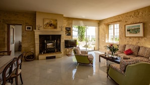 A cozy living room with a fireplace, a green armchair, a patterned sofa, and a dining area with chairs and a table.