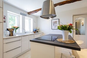A modern kitchen with a central island, a hanging light fixture, and a vase with flowers. - Stone Cabin with Swimming Pool - King-Size Beds & Views of the Pyrenees (Gondrin)
