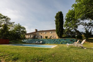 A stone house with a swimming pool, surrounded by grass and trees.
