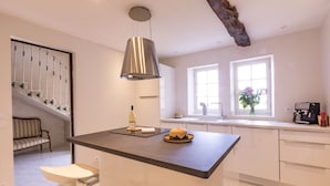 A modern kitchen with a central island, a hanging light fixture, a staircase, and a window with flowers.