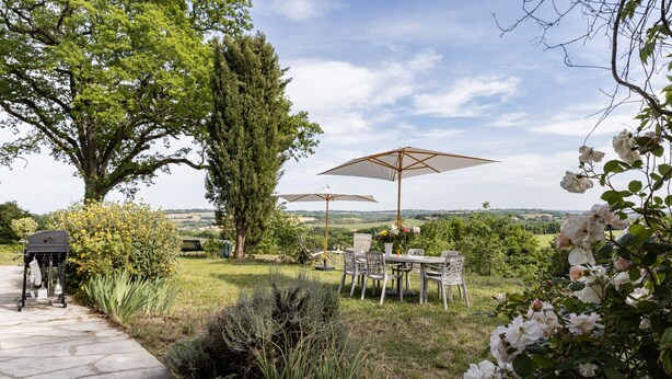 An outdoor seating area with stone flooring, a grill, and a view of the countryside.