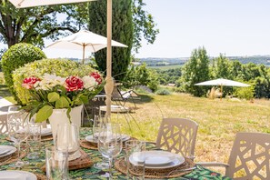 Un espacio exterior de comedor con mesas dispuestas para una comida, rodeado de follaje y una vista panorámica.