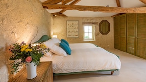 A bedroom with a wooden ceiling, a bed with white bedding, a small window, and a mirror on the wall.