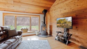 A cozy living room with a leather sofa, a flat-screen TV, and a wood-burning stove.