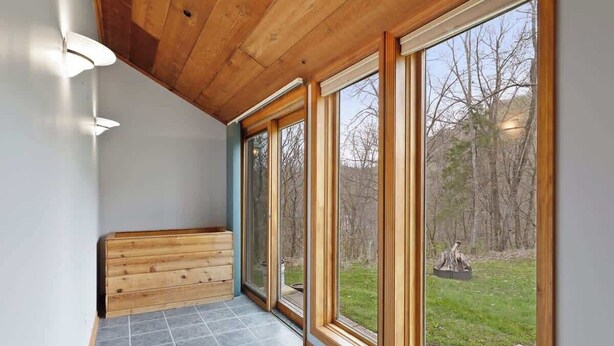 A modern interior with large windows, a wooden bench, and a tiled floor.
