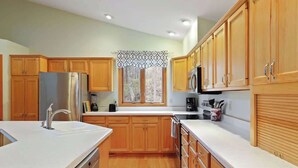 A kitchen with wooden cabinets, a stainless steel refrigerator, a microwave, and a window with a decorative valance.