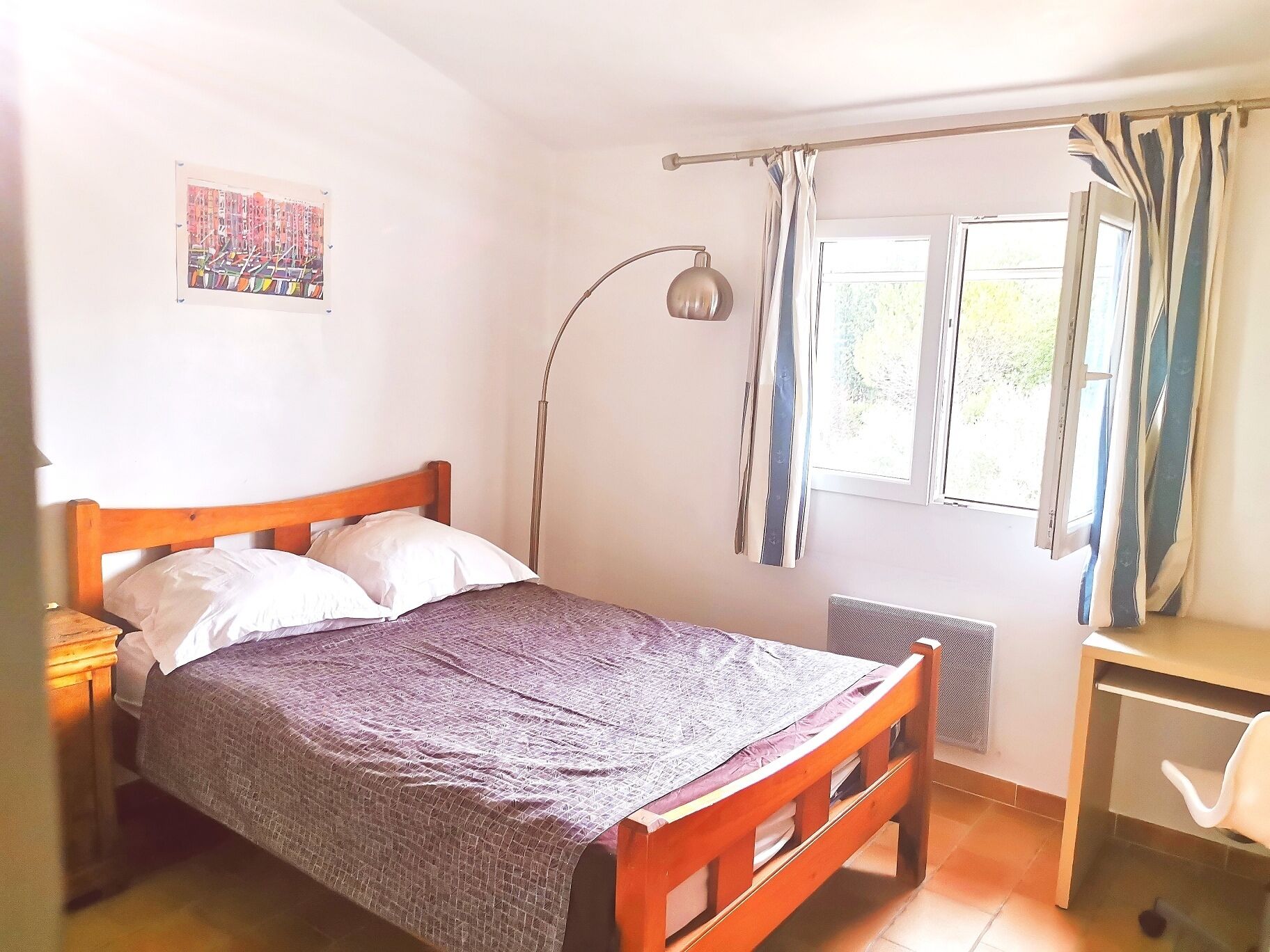 Un dormitorio con cama de madera, un escritorio, una lámpara de pie y una ventana con cortinas.