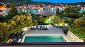 A pool area with lounge chairs and a view of a town by the water. - Private stone villa on the island for 10 people with pool and sea view (Prvic Luka)