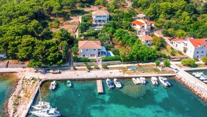 An aerial view of a coastal area with several buildings, a marina with boats, and a clear turquoise sea. - Private stone villa on the island for 10 people with pool and sea view (Prvic Luka)