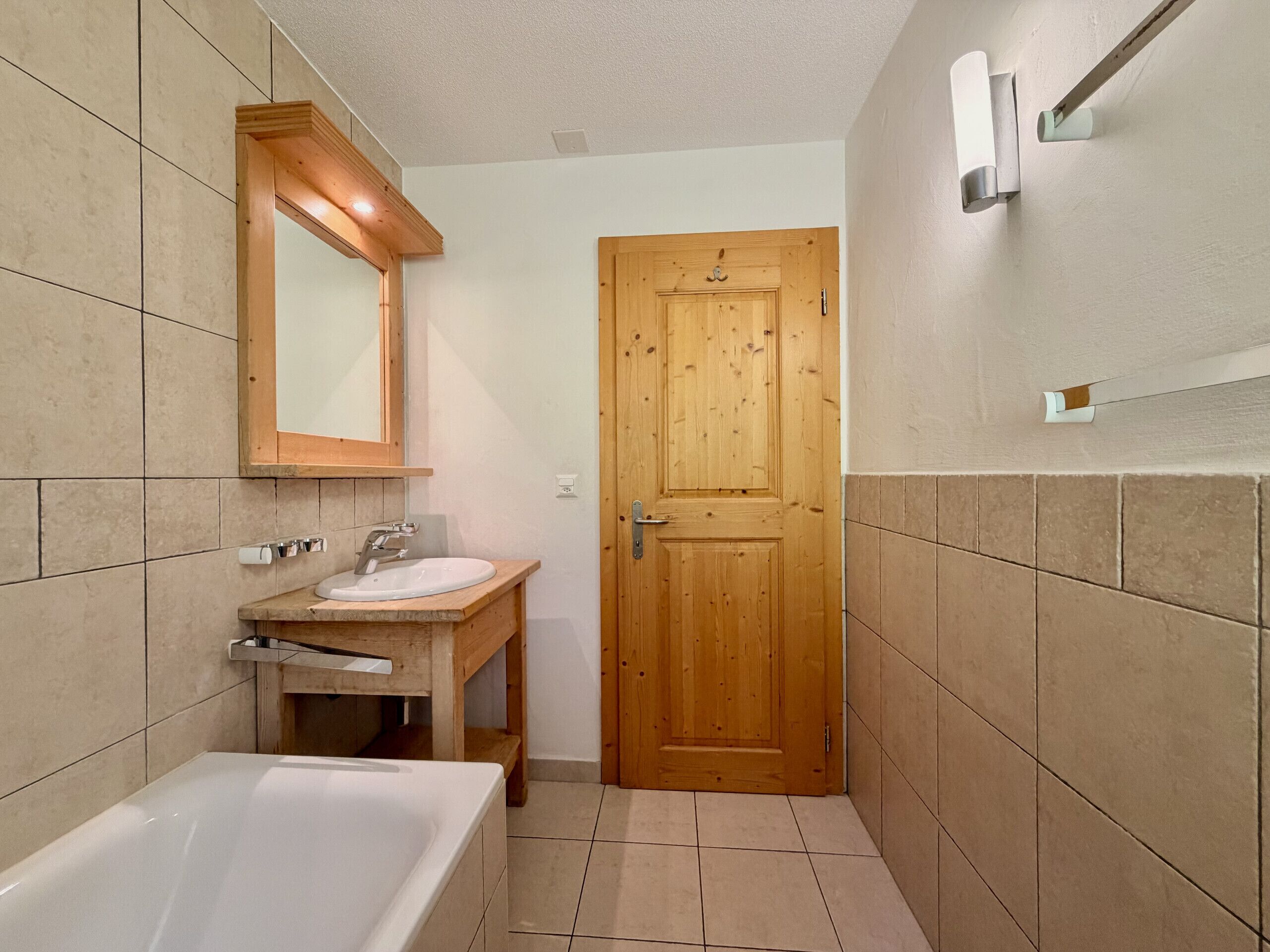 Une salle de bain avec une porte en bois, un lavabo, un miroir et une baignoire.