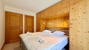 Een slaapkamer met een houten garderobe, een bed met witte lakens en een vloerbedekking.