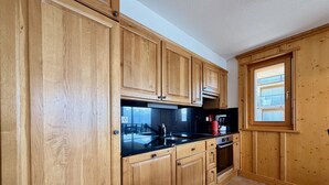 Een keuken met houten kastjes, een zwart aanrecht, een fornuis en een raam met zonwering.