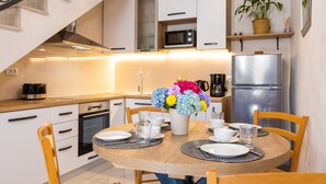 Una cocina moderna con armarios blancos, un refrigerador de acero inoxidable, un microondas y una estufa. Hay una mesa de comedor con platos, tazas y un florero.