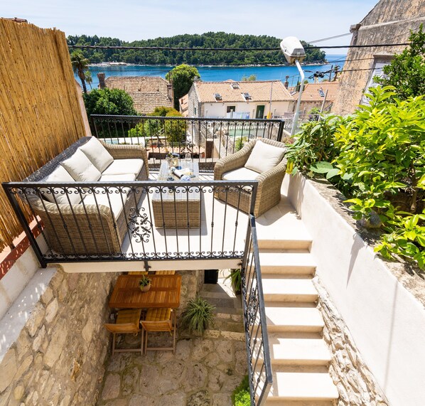Una terraza en la azotea con muebles de mimbre, una mesa de madera y vistas a un pueblo costero y al mar.