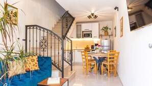 Un apartamento moderno con una escalera, una sala de estar con un sofá azul, un comedor con sillas de madera y una cocina con armarios blancos y un microondas.