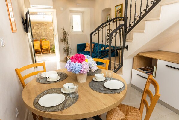 A dining area with a round wooden table set for four, surrounded by wooden chairs. A vase with colorful flowers is placed in the center.