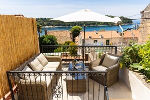 A balcony with wicker furniture, a white umbrella, and a view of the sea and buildings. - Cozy stone house with lovely view in Cavtat centre (Cavtat)