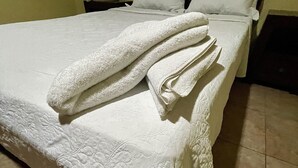 Een opgemaakt bed met een witte spreideken en kussens, een nachtkastje met een lamp, en een betegelde vloer.