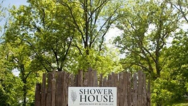 A wooden structure labeled "SHOWER HOUSE" with a metal faucet and a wooden bench in front. - Lost Hill Lake Charming Camper (Central Township)