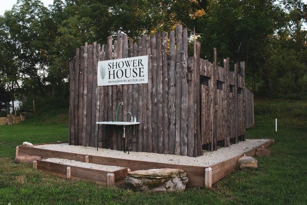 Une structure en bois portant l’inscription « Douches » et comprenant un lavabo, ainsi qu’une pancarte indiquant : « Offert par Better Life ».