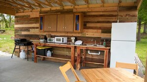 A rustic wooden cabin with a kitchen area featuring a grill, microwave, and refrigerator. - Lost Hill Lake Charming Camper (Central Township)