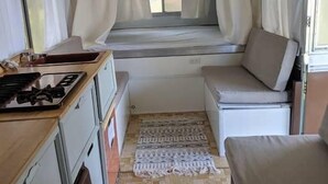 A compact RV interior with a kitchenette, a small seating area, and a window with curtains. - Lost Hill Lake Charming Camper (Central Township)