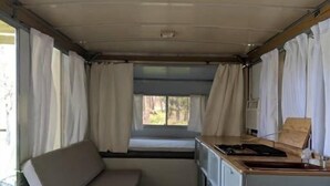 A compact RV interior with a kitchenette, a small seating area, and a window providing natural light. - Lost Hill Lake Charming Camper (Central Township)