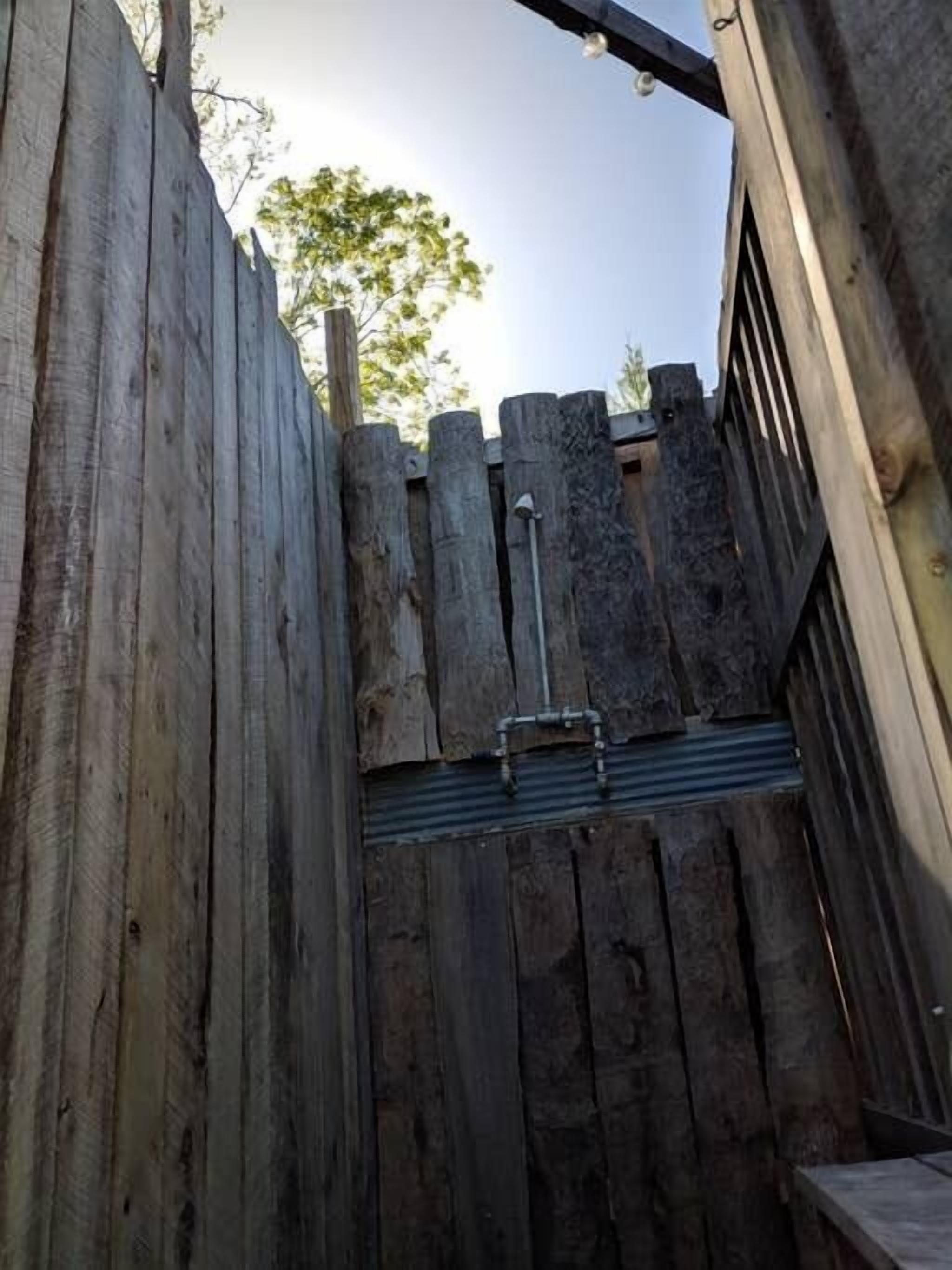Una tanca de fusta amb una porta metàl·lica, un pont de fusta i un arbre al fons.