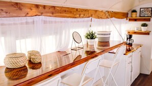 Een compacte keuken met een houten aanrecht, witte stoelen, een koffieapparaat en een spiegel die aan de muur hangt.