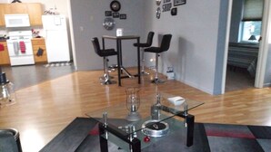 A modern kitchen with a microwave, oven, and refrigerator. There is a dining area with two black chairs and a table. The room has a wooden floor and a patterned rug. - "THE SHOP" retro 60's (Keosauqua)