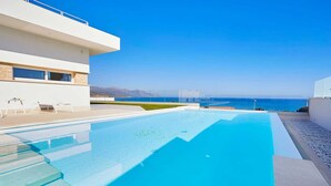 A modern pool area with clear blue water, a view of the ocean, and a contemporary building with large windows. - VILLA DARDA (Alcamo)