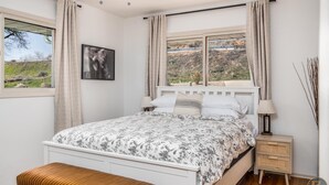 Une chambre à coucher avec un lit, une table de chevet, une lampe et une fenêtre avec des rideaux.