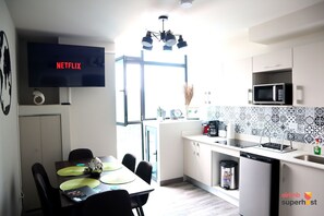 A modern kitchen with a flat-screen TV displaying 'NETFLIX', a dining area with a table and chairs, and a view through a large window. - Apartamento Lujoso en Rohrmoser al mejor precio (San José)