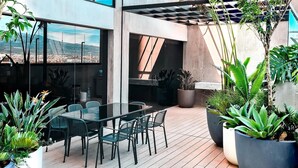 Eine moderne Terrassenanlage im Freien mit einem Glastisch und Stühlen, umgeben von üppigen Kübelpflanzen und Blick auf die Stadt.