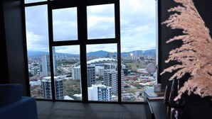 Ein Zimmer mit großem Fenster und Blick auf die Stadt, ein blauer Sessel und eine Zierpflanze.