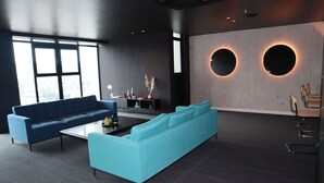 Ein moderner Büroraum mit zwei Sofas, einem Couchtisch und einem Schreibtisch mit Lampe. Zwei runde Wanddekorationen und ein Fenster mit Blick auf die Stadt.
