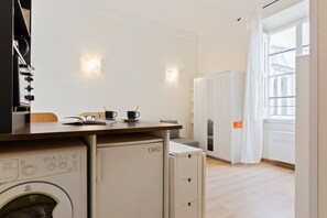 A compact kitchen with a washing machine, a small refrigerator, and a dining area with a table and chairs.