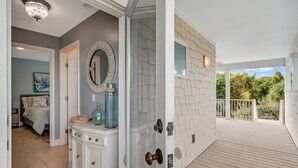 Une pièce avec une coiffeuse blanche, un miroir et une porte donnant sur un balcon avec vue sur les arbres.