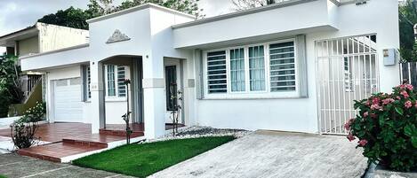 A modern two-story house with a garage, a small front yard with a paved area, and a gated entrance.