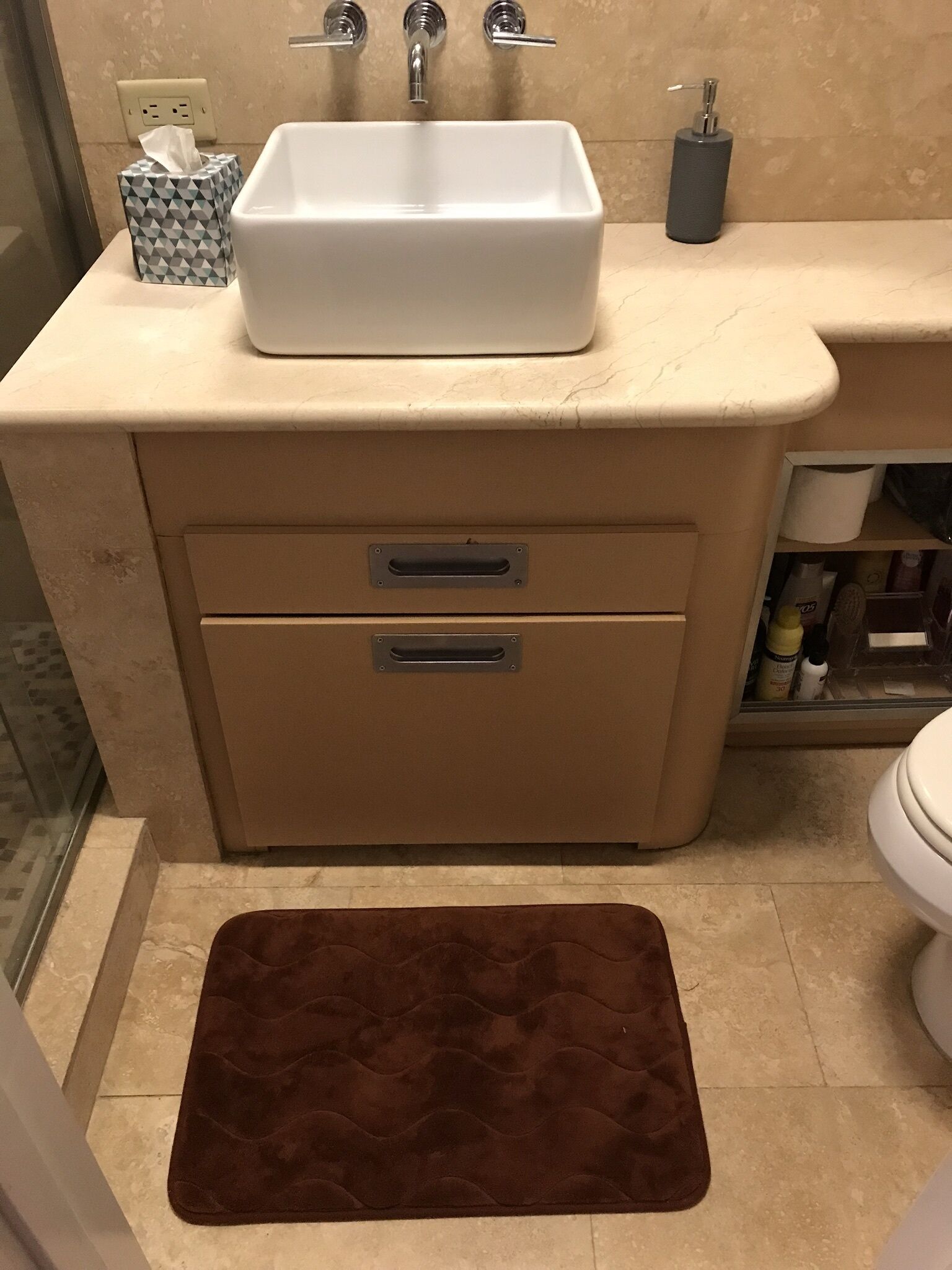 Un baño con lavamanos blanco, dos cajones, un perchero y una alfombra de baño marrón.